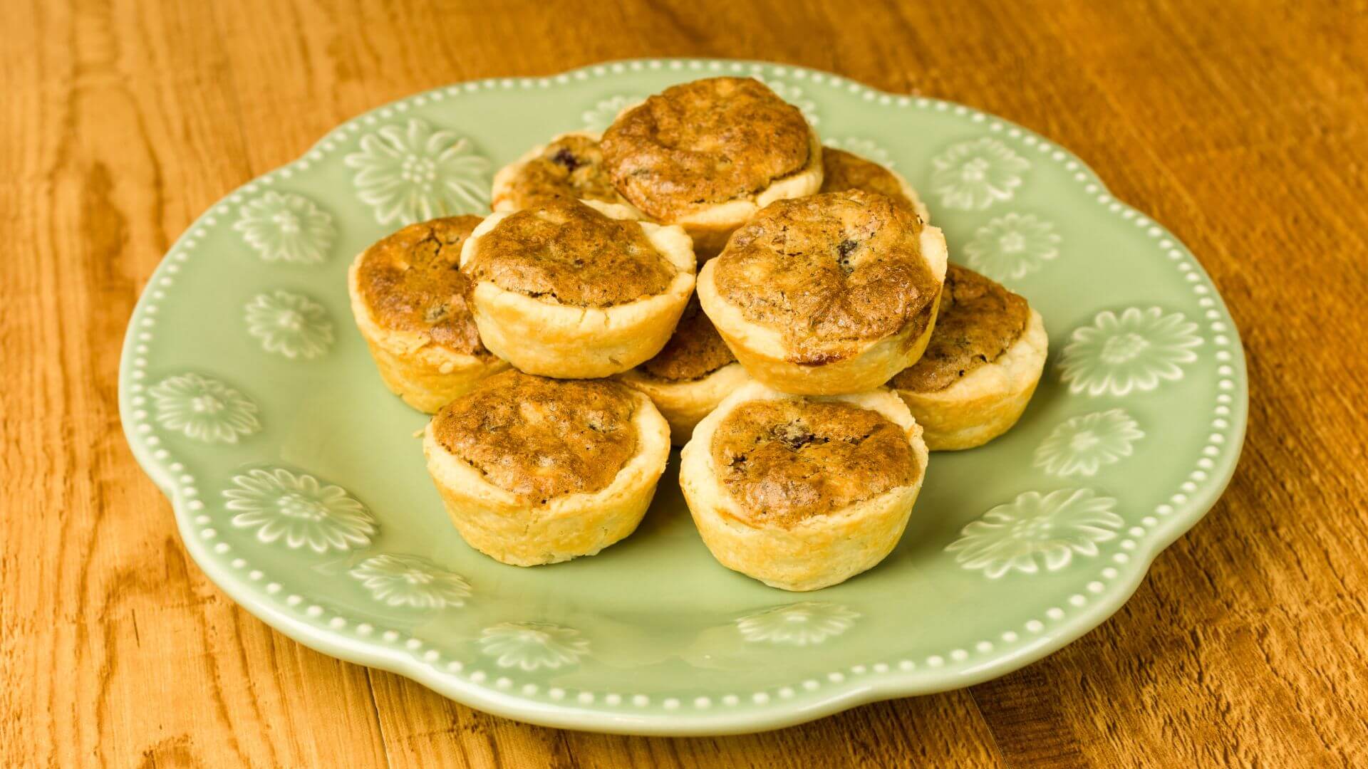 Mini pecan pies on a light green plate on a wood table.
