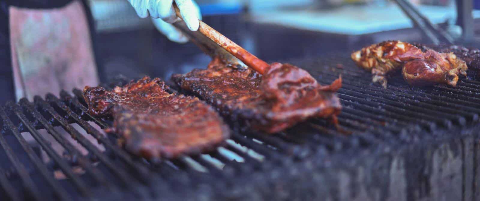 ribs on a BBQ grill with someone spreading sauce over them