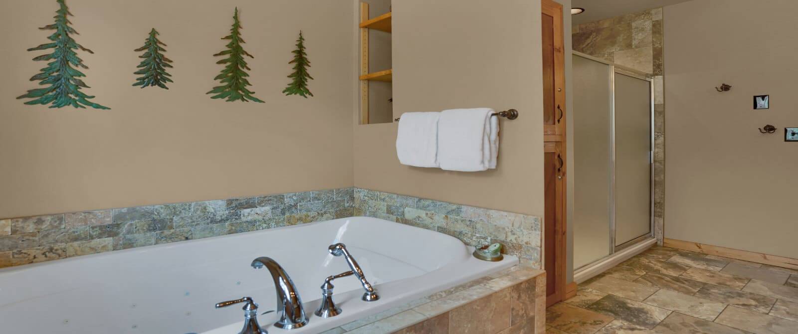 jetted tub with metal trees on the wall, and a large shower at the end of the wall.