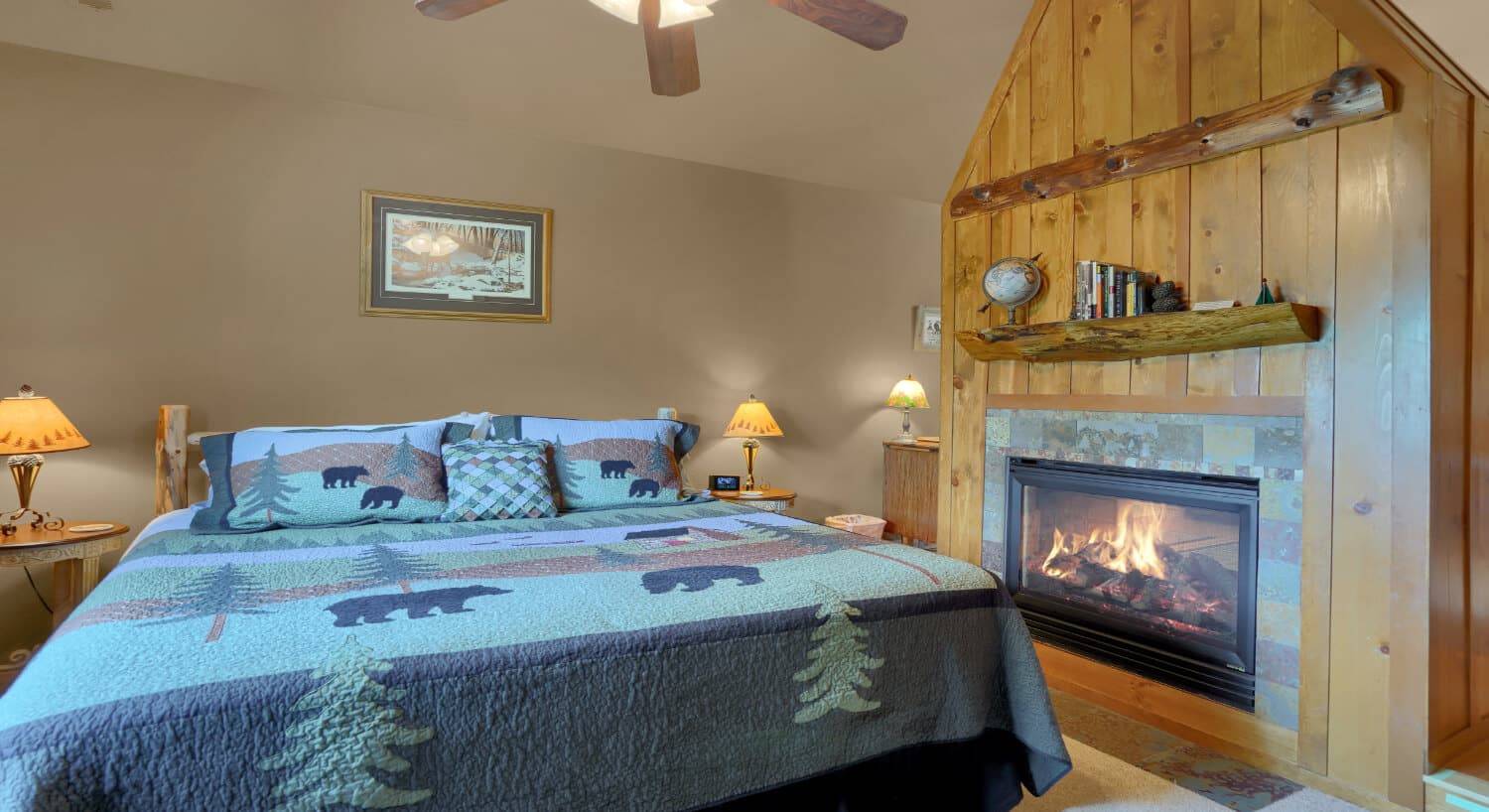 A king bed with a blue quilt with pine trees and bears, and a fireplace to one side.