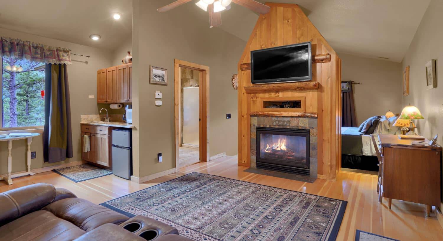 sitting room with fireplace, large flat screen tv, a bed in a back room, and a small kitchenette