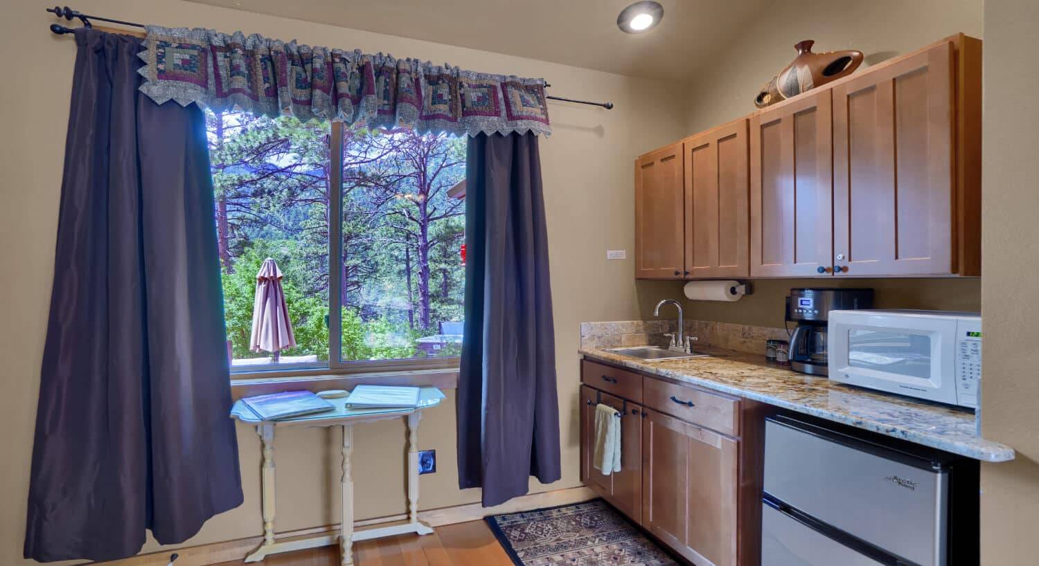 a small kitchen area with mini fridge, microwave, coffeemaker, and large picture window with trees and mountains