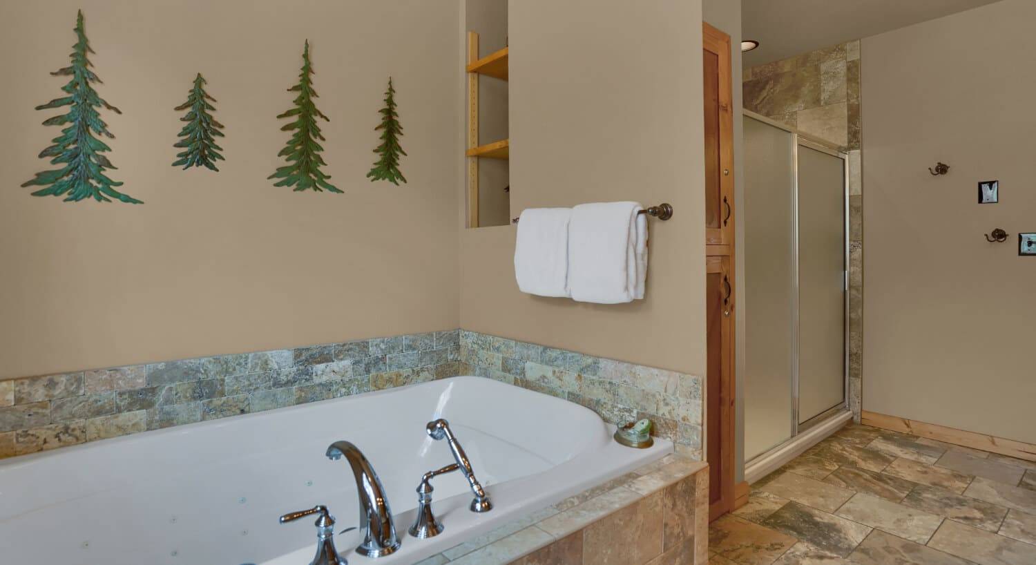 a deep jetted tub for two with green pine trees on the wall and a large walk in shower next to it