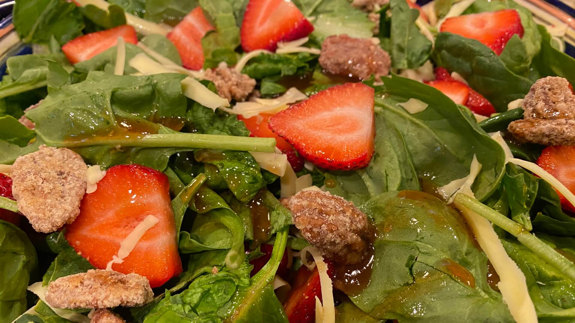 a fresh salad with green spinach leaves, sliced red strawberries, slivers of monterey jack cheese, and sugar-cinnamon coated pecans.