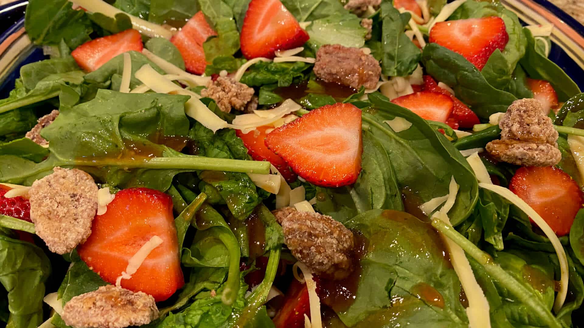 A salad with fresh spinach leaves, strawberry slices, grated Monterey Jack cheese, candied pecans, and a raspberry vinaigrette dressing