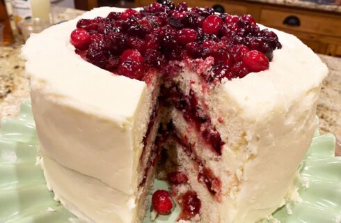 layered white cake with a cranberry filling, frosted with a white frosting and topped with more cranberry topping.