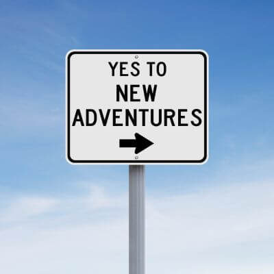 a white sign in front of a blue sky that says Yes to New Adventures with an arrow